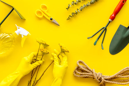 Rake, spade, scissors, spray, rope, hands in gloves. Gardening tools on yellow background top view...