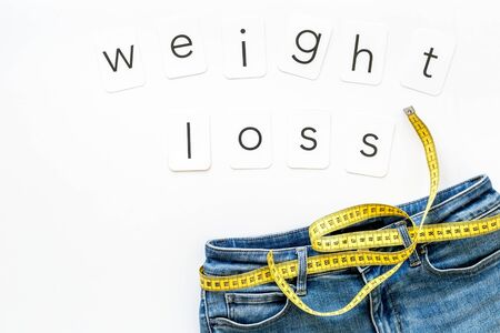 pants and measuring tape for weight loss with text on white background top view space for text