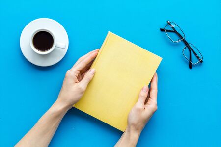 Reading books in hands with glasses and coffee on blue library desk background top viewの写真素材