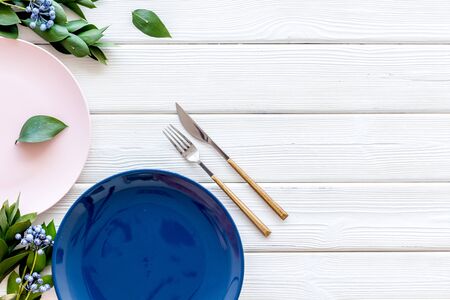 Table setting with plates, flatware and flower on white wooden background top view copy space
