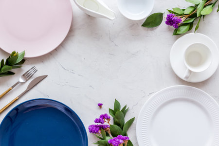 Table setting with plates, flatware and flower on marble background top view copy space