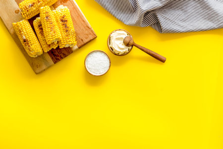 Fried corn on board with salt and butter on yellow background top view mock up