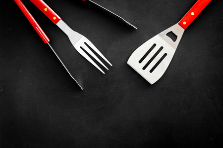 spatula, fork, tongs for barbecue on black background top view mock up