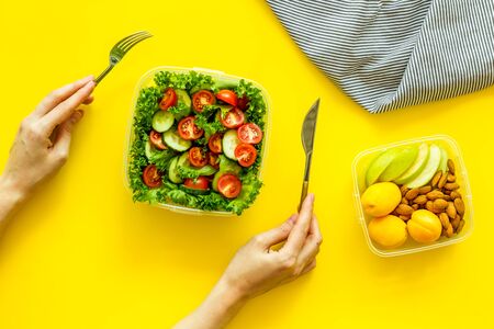 salad to go in lunch box and hands with flatware on yellow background top viewの写真素材