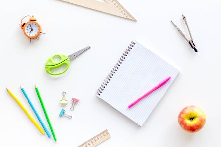 Students desk with stationery, apple, alarm clock, textbook on white background top viewの写真素材