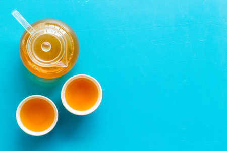 Tea brewing in pot and cups on blue background top view space for text