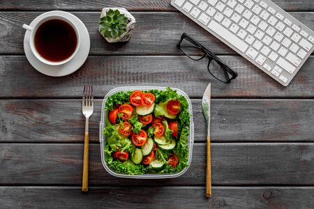 Healthy dinner in lunch box near keyboard and tea on wooden background top viewの写真素材