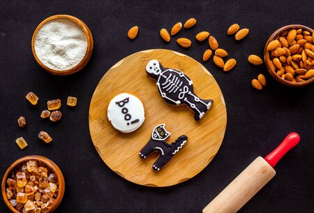 Cooking halloween cookies in shape of spooky figures, rollin pin, nuts and flour on black background top viewの写真素材