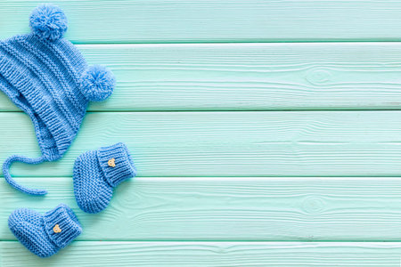 Knitted blue footwear and hat for baby boy on mint green wooden background top view mockupの写真素材