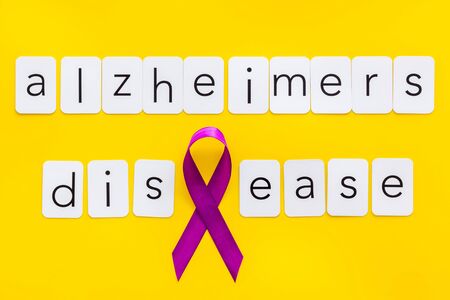 Alzheimers disease text near violet ribbon on yellow background top viewの写真素材