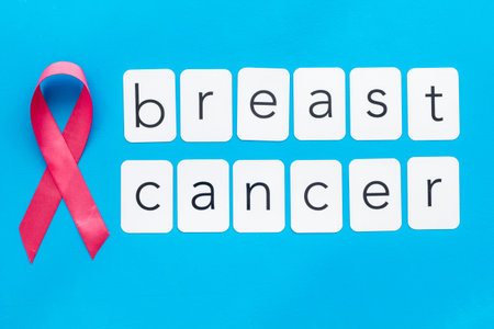 Pink ribbon as symbol of breast cancer awareness on blue background top view