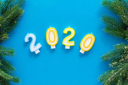 2020 New Year design. Date laid out by candles near fir branches on blue background top view copy...