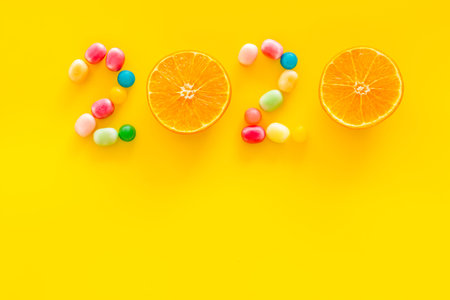 Sweet New Year design. 2020 laid out with candy and oranges on yellow background top view.