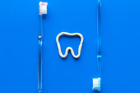 Teeth brushing concept. Tooth drawn with toothpaste near toothbrushes on blue background top view
