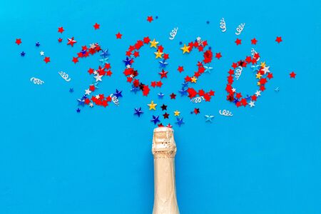 Celebrate New Year 2020. Date on confetti near champagne bottle on blue background top view copy spaceの写真素材