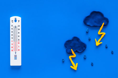 Rainy weather. Thermometer near clouds and drops on blue background top view copy space