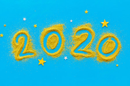 2020 Happy New Year. Date written on golden dust on blue background top view