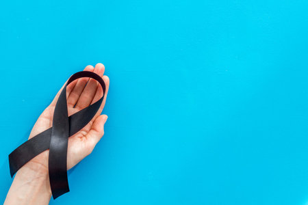 Disease control concept. Black ribbon in hands on blue background top view copy space