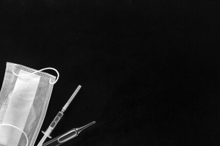Influenza preventive tools. Medical face mask and vaccine on black background top view copy spaceの写真素材