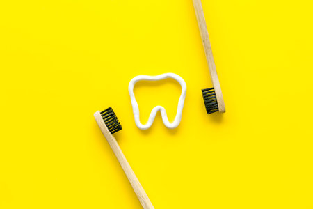 Teeth brushing concept. Tooth drawn with toothpaste near toothbrushes on yellow background top view...