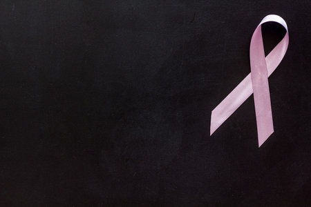 Pink ribbon as symbol of breast cancer awareness on black background top view