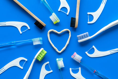 Oral hygiene concept. Heart drawn with toothpaste near toothbrushes on blue background top view.