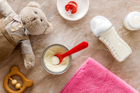 Make mixture for feed baby. Spoon with food in hand near toys and accessories on brown background...