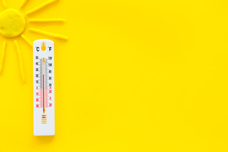 Sunny weather concept. Sun and thermometer on yellow background top view.