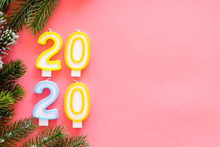 2020 New Year design. Date laid out by candles near fir branches on pink background top view.
