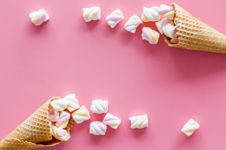 Sweet desserts. Marshmallows in ice cream waffle cone on pink background top view.