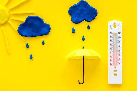 Rainy weather. Thermometer near clouds and drops on yellow background top view.の写真素材