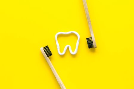 Teeth brushing concept. Tooth drawn with toothpaste near toothbrushes on yellow background top view.の写真素材
