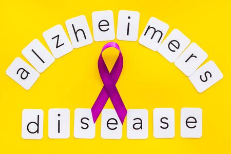 Alzheimers disease text near violet ribbon on yellow background top view.の写真素材