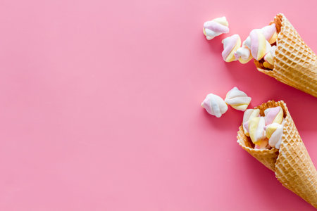 Sweet desserts. Marshmallows in ice cream waffle cone on pink background top view.