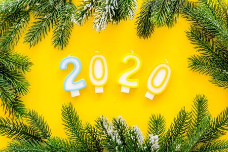 2020 New Year design. Date laid out by candles near fir branches on yellow background top view.の写真素材