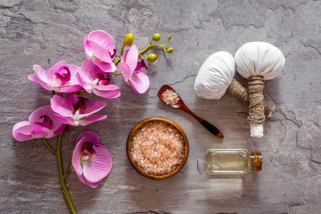 Massage table with thai herbal balls and orchids on grey background top view patternの写真素材
