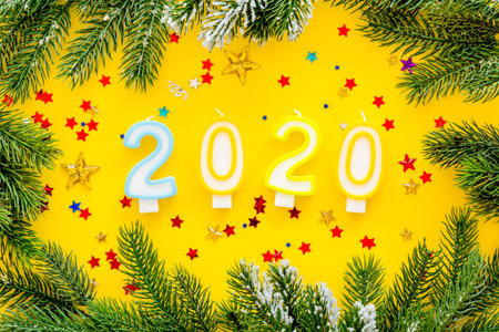 2020 New Year design. Date laid out by candles near fir branches on yellow background top view