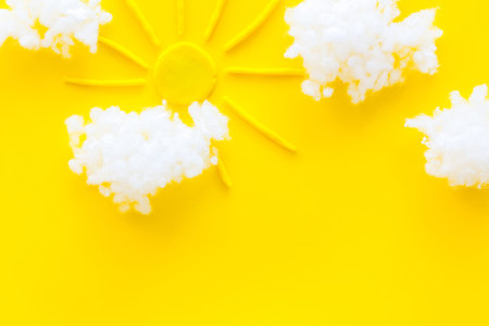 Cloudly weather concept. Sun and clouds on yellow background top view.
