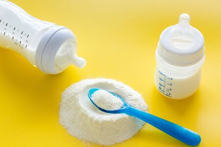 Baby food. Powder in spoon near baby bottle on yellow background.の写真素材
