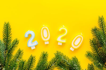 2020 New Year design. Date laid out by candles near fir branches on yellow background top view.の写真素材