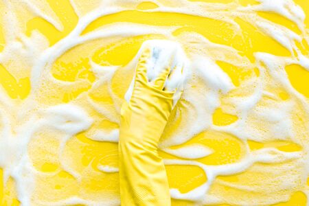 Washing concept. Hand in rubber glove and foam backgroud on yellow table top view copy spaceの写真素材