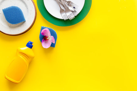 Dishwashing liquid bottle near plates on yellow background top view space for text