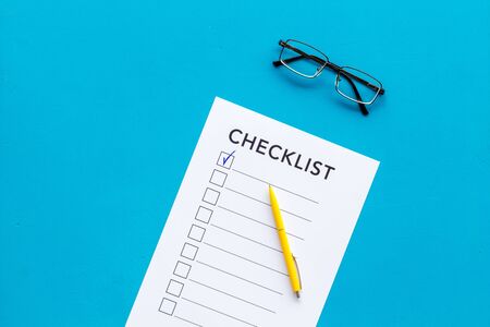 Checklist and pen on blue background top view.