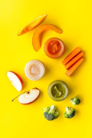 Baby food. Colorful puree in glass jars near vegetables and fruits on yellow background top view.の写真素材