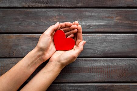 Heart icon. Paper heart in hands on dark wooden background top view.の写真素材