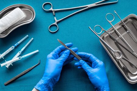Preparing for plastic surgery. Doctor's hands takes scalpel on blue background with surgical tools top view.の写真素材