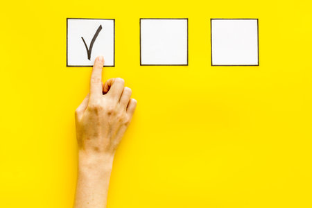 Hand put check mark in check-box on yellow background top view.