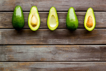 Avocado pattern - halfs of fruit - on dark wooden background top view copy space