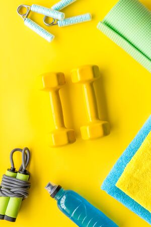 Fitness background - dumbbells, jump rope, sport carpet, water bottle - on yellow top-down.の写真素材
