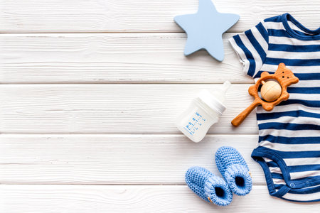 Clothes and accessories for newborn boy on white wooden table top-down frame copy space